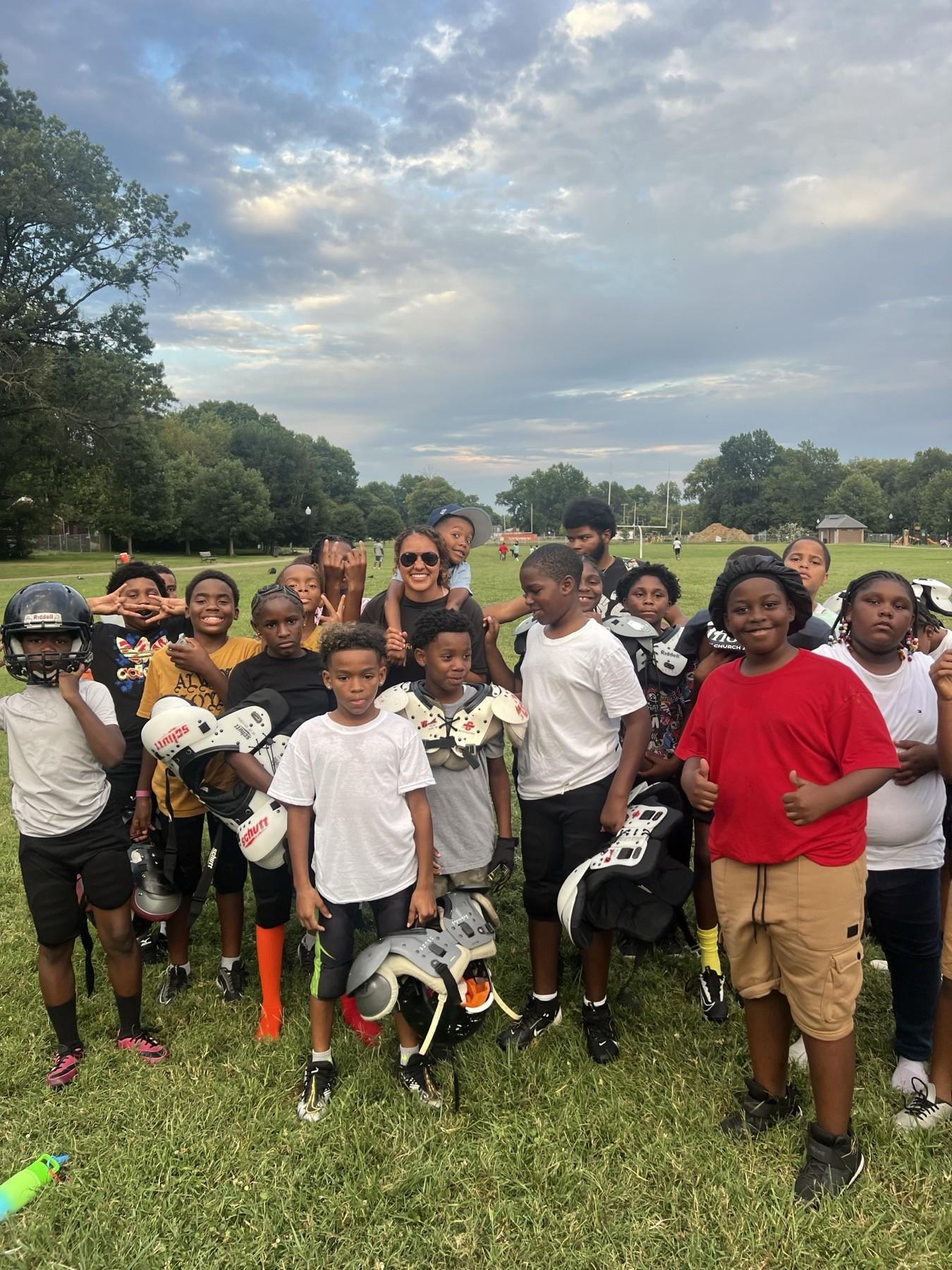 A youth football team in full pads standing with their Huddle coach at a Louisville park
