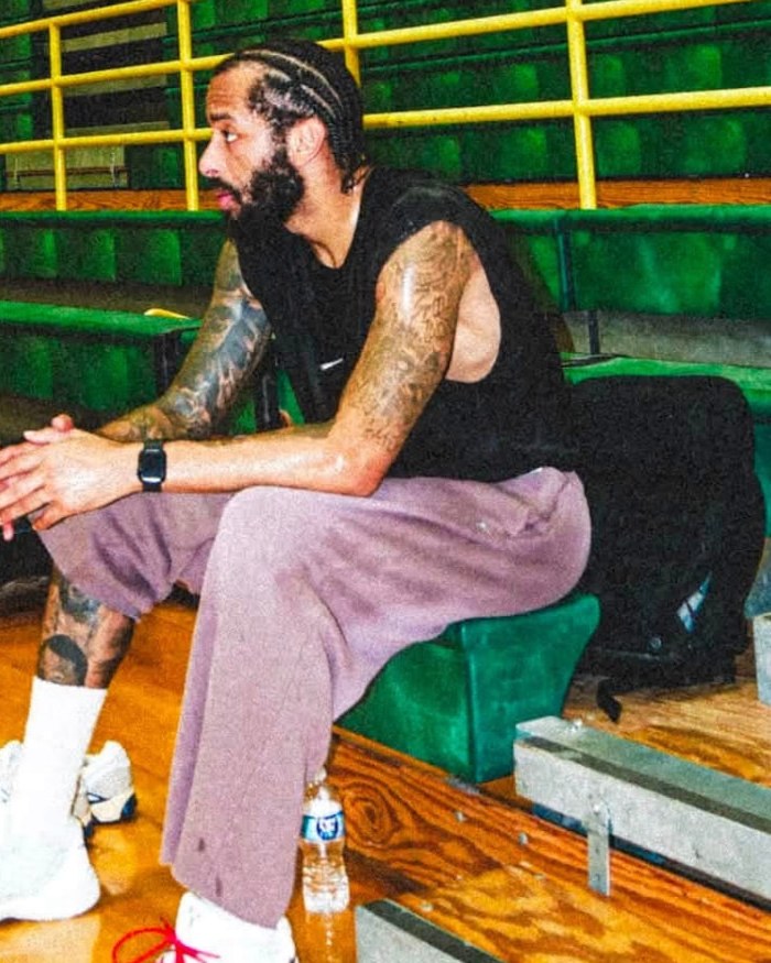 Terran Petteway, trainer and coach for The Huddle Inc., seated on gym bleachers talking with a young basketball player