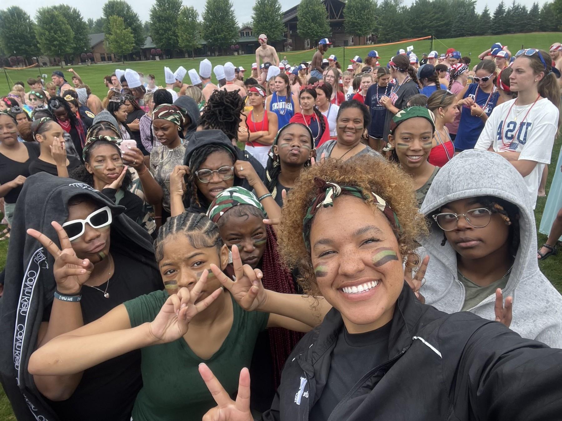 A large group of young people at a Huddle camp field day, many wearing camo face paint and headbands