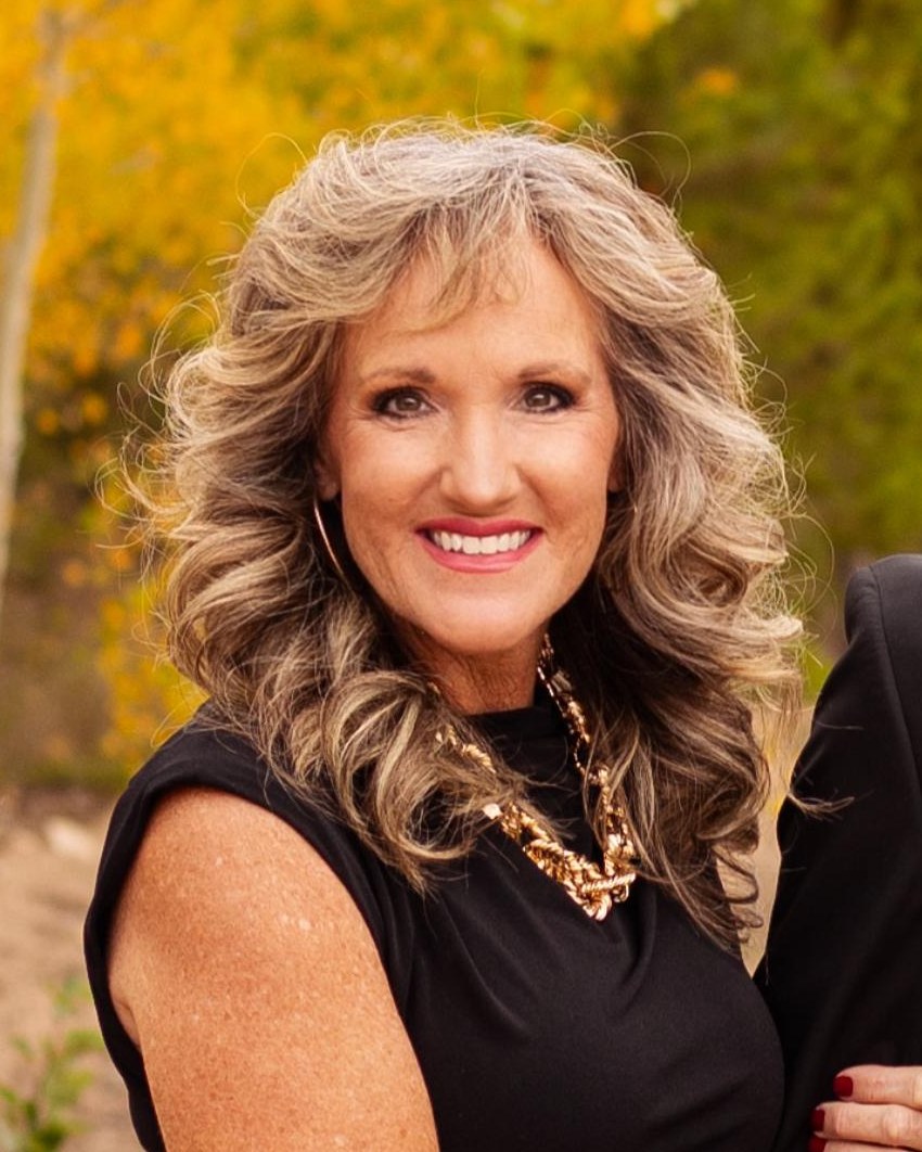 Beth Pringle, General Manager of The Huddle Inc., smiling outdoors in a black dress in front of autumn trees