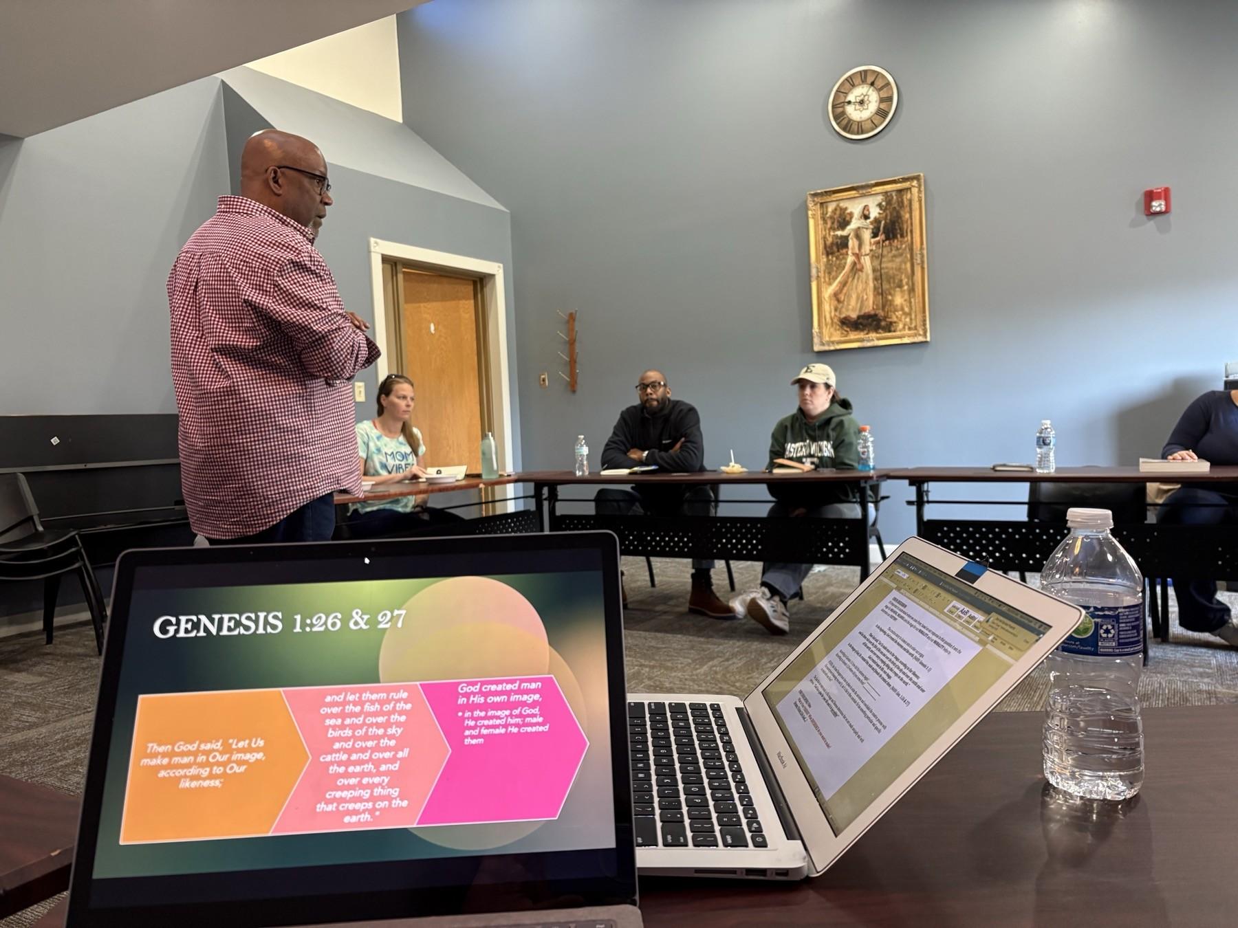 A Purpose Playbook facilitator presenting Genesis scripture slides to adults seated at tables in a classroom