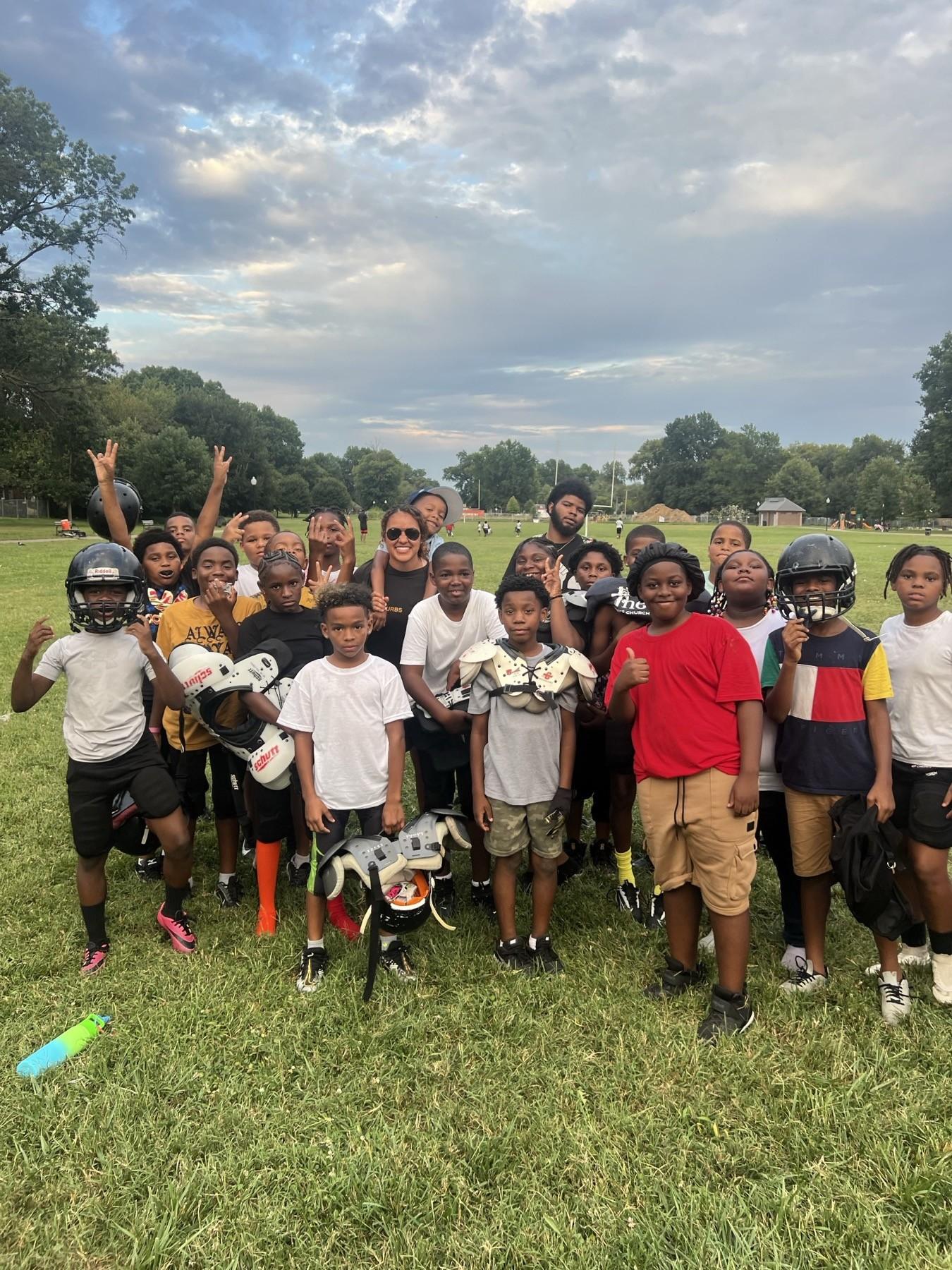 A youth football team and their Huddle coach gathered together on a field at a Louisville park
